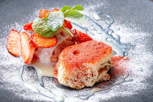 黒い皿に盛り付けられた、イチゴと赤いパウダーがかけられたデザート