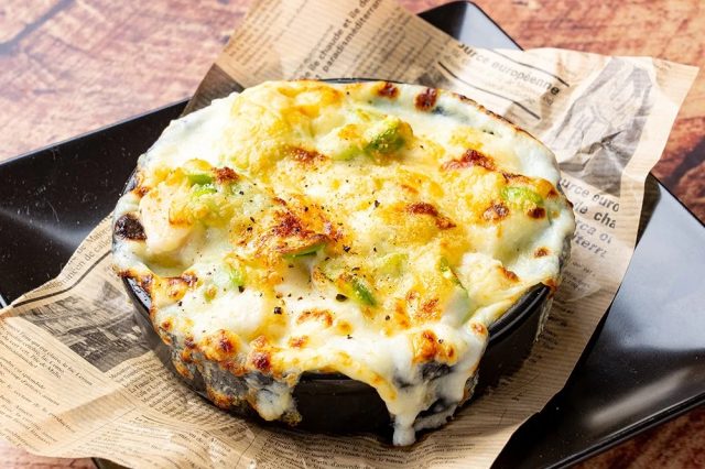 黒い器に入った熱々のグラタン。とろけるチーズがこんがりと焼き上げられ、アボカドやエビのような具材が見える