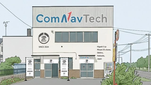 北海道帯広市にある「ComNavTech」と「HOSAC」のロゴが特徴的な建物の外観です。2024年創業で、自動操舵技術「HOSAC」に関する旗が立てられています。