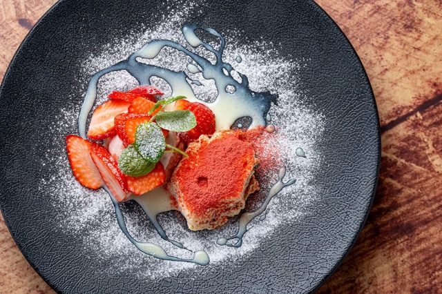 黒い皿に盛り付けられた、イチゴと赤いパウダーがまぶされたデザート