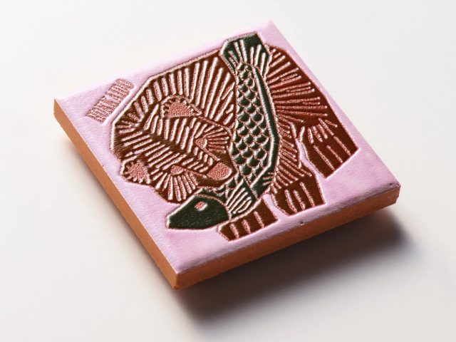 ピンク色の表面に、魚と放射状の模様が立体的に刻まれた正方形のブロック
